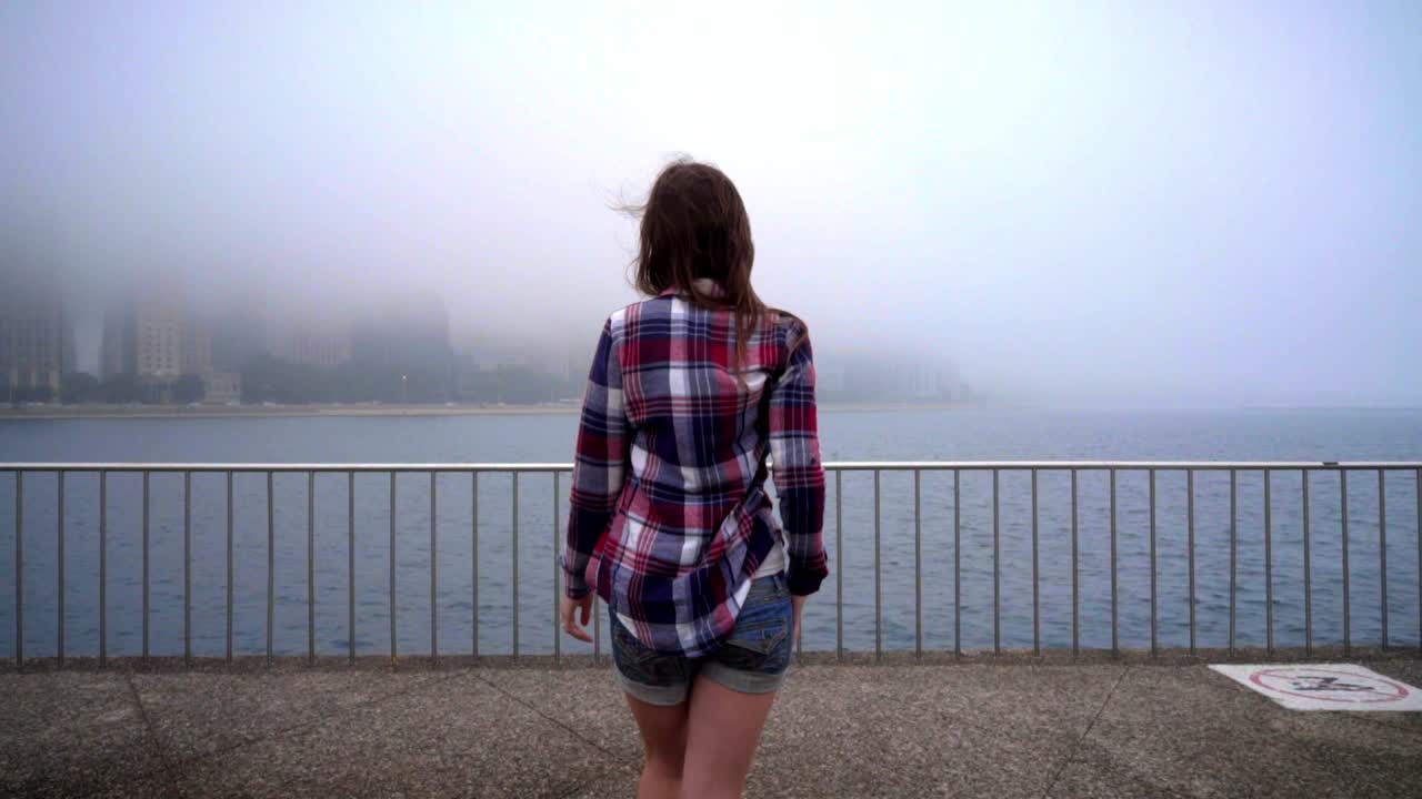 Donna che cammina e osserva la nebbia sulla città di mare. Donna che si dirige verso il mare in città.