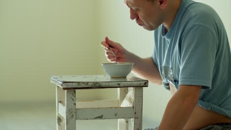 A man eats noodles while sitting at an old and dirty chair, on a light background