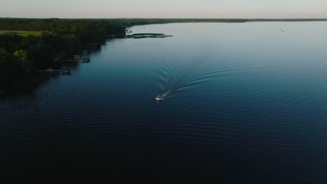 Umkreisende-Drohnenaufnahme-Eines-Pontons-Mit-Einer-Kleinen-Spur-Auf-Einem-See-Bei-Sonnenuntergang