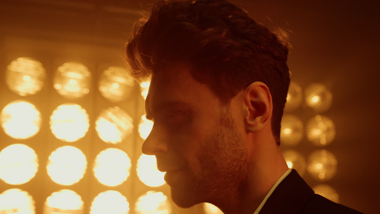 남자 모델이 스포트라이트에서 프로필을 보여줍니다. 클럽에서 포즈를 취하는 매력적인 남자.