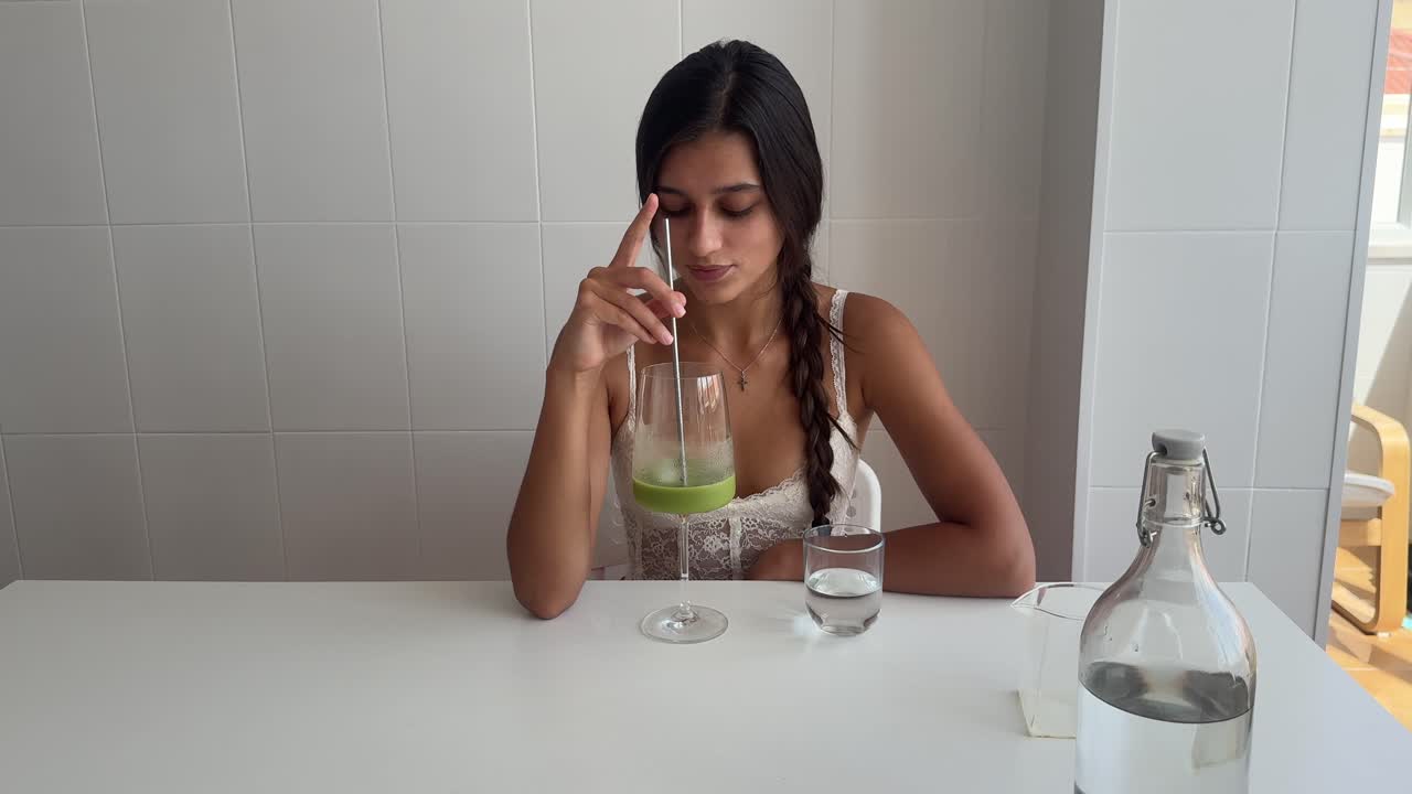 Giovane donna che beve succo verde a un tavolo bianco