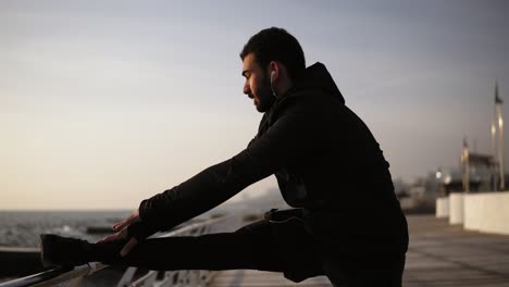 un joven deportivo estirándose en el muelle cerca de la orilla del mar. hermosa mañana soleada en la costa. imágenes al aire libre.