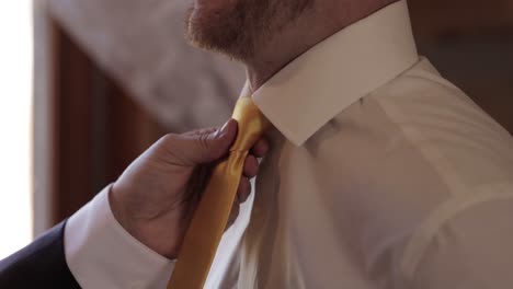 padrino apretando una corbata amarilla de novios en preparación para su ceremonia de boda