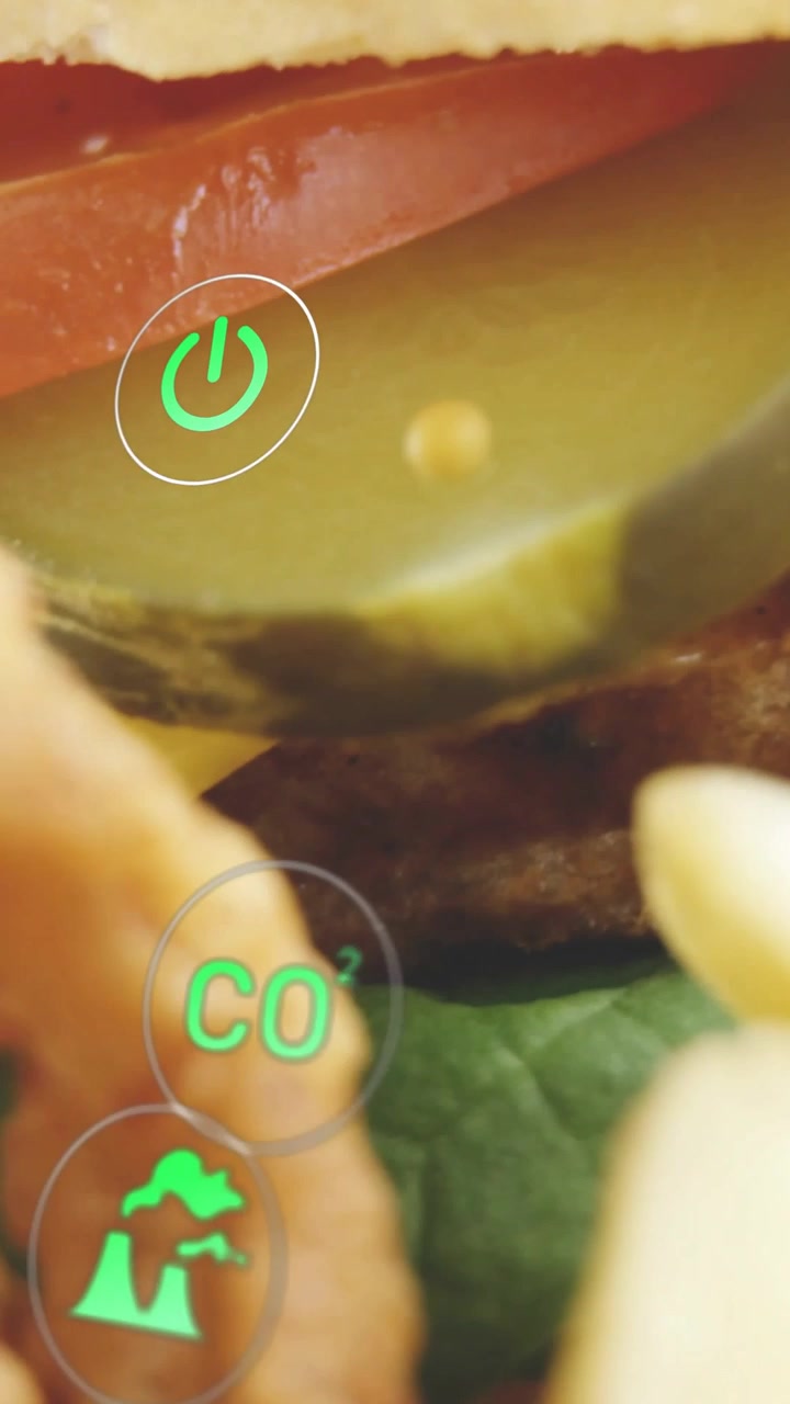 Video verticale: Hamburger che rivela i suoi strati, cetriolino che spunta, anelli che scorrono, icone ecologiche che mostrano dati.