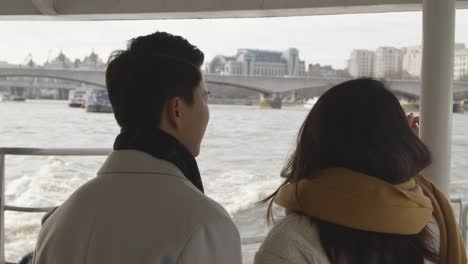 young asian couple on holiday taking trip on thames river boat in london uk 1