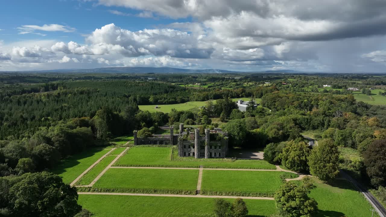 Castle Saunderson, County Cavan, Ireland, September 2022. Drone orbits clockwise in a wide aerial view of Gothic Revival Castle surrounded by lush green forest with the Finn River in the background.