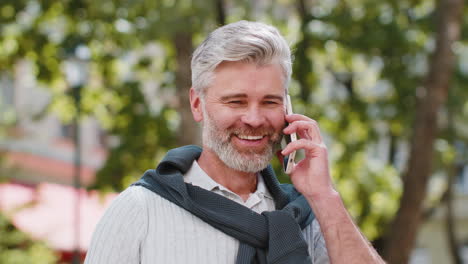 Mature-tourist-man-having-remote-conversation-online-talk-by-smartphone-unexpected-good-news-gossip