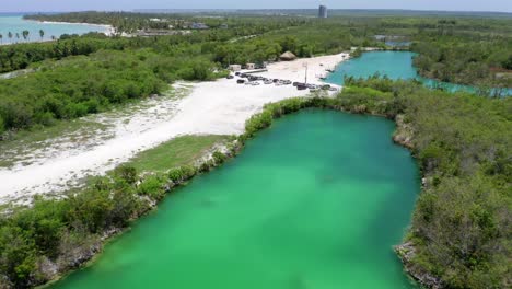 Forward-flight-with-view-of-the-blue-lake,-cap-cana,-car-parked,-view-of-the-beach-in-the-background