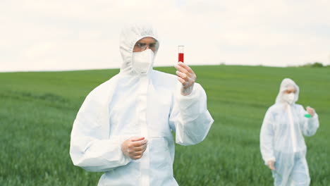 caucasian researcher man in protective suit holding test tube while doing pest control in the green field