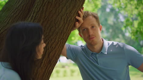 hombre tranquilo hablando con su esposa inclinado sobre un árbol de cerca. retrato de una familia descansando