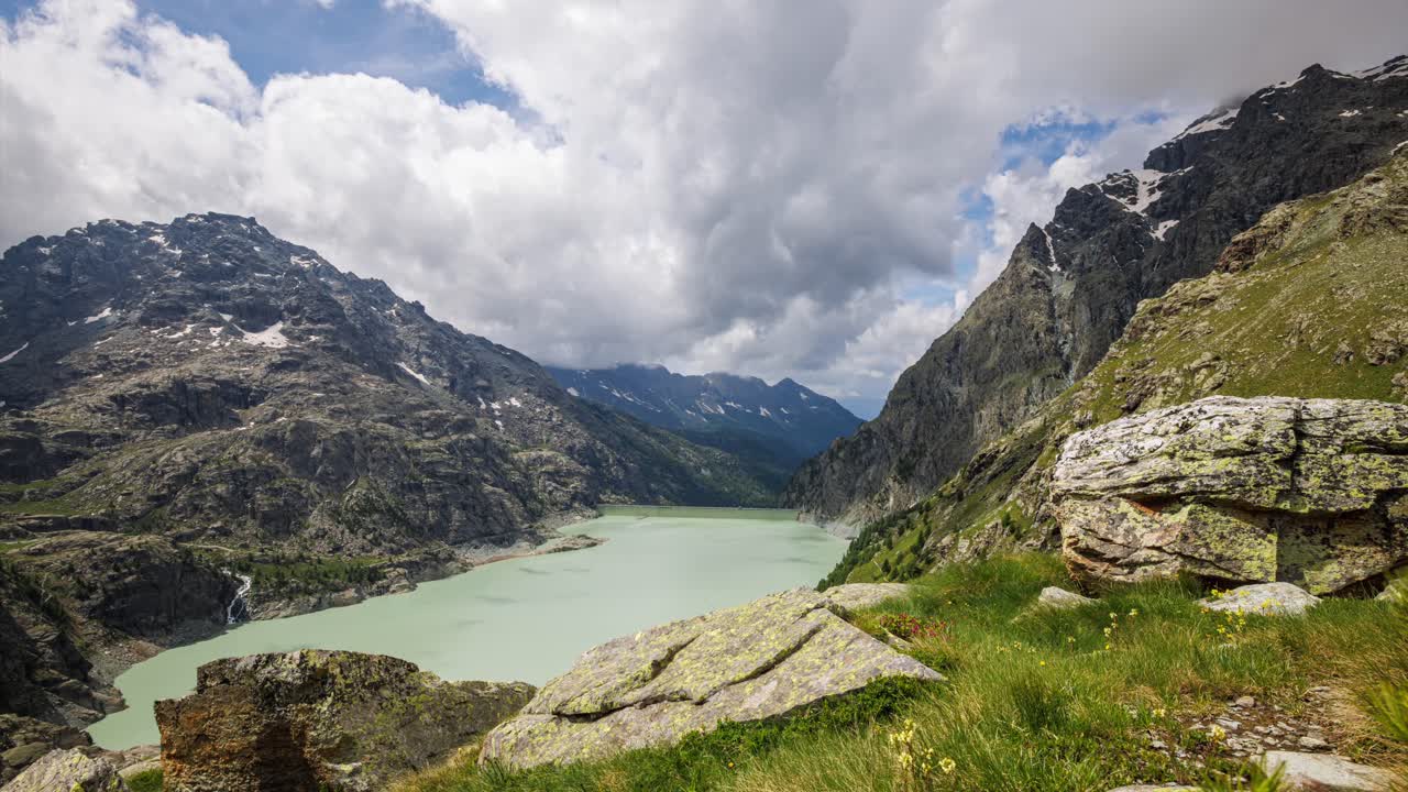 Timelapse video of the scenic Diga dell'Alpe Gera in the Italian Alps, showcasing serene mountain views, a turquoise lake