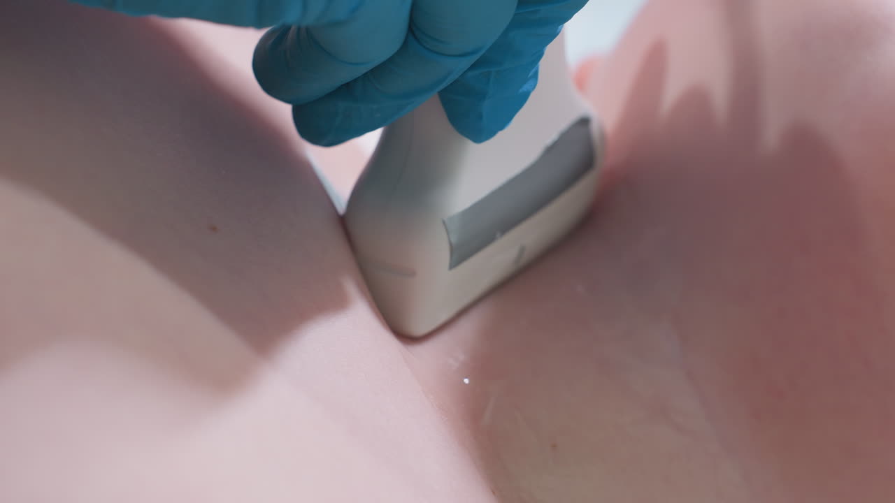 Clinical laboratory scientist wearing blue gloves carefully moves ultrasound scanner over throat region of smooth skinned young boy with gel applied to ensure clear imaging diagnostic procedure