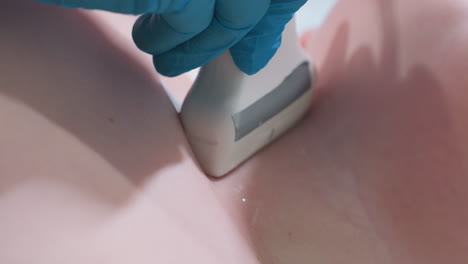 clinical laboratory scientist wearing blue gloves carefully moves ultrasound scanner over throat region of smooth skinned young boy with gel applied to ensure clear imaging diagnostic procedure