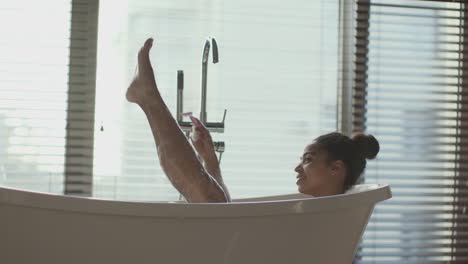woman relaxing and shaving legs in bathtub