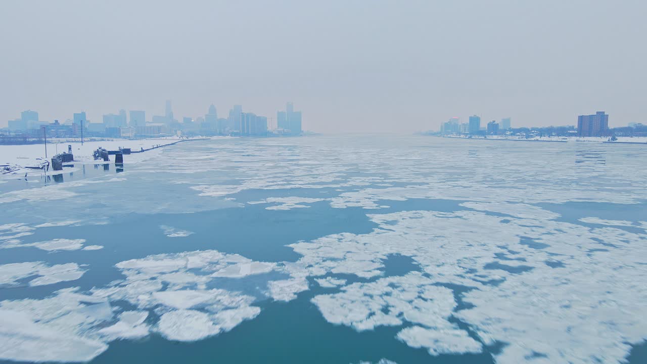 Floating ice drifts along frozen Detroit River with city skyline in cold winter haze