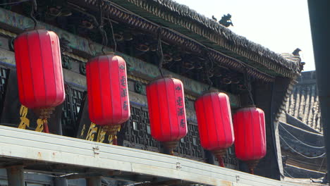 chinese red lanterns hanging from a roof of traditional house moving in the wind