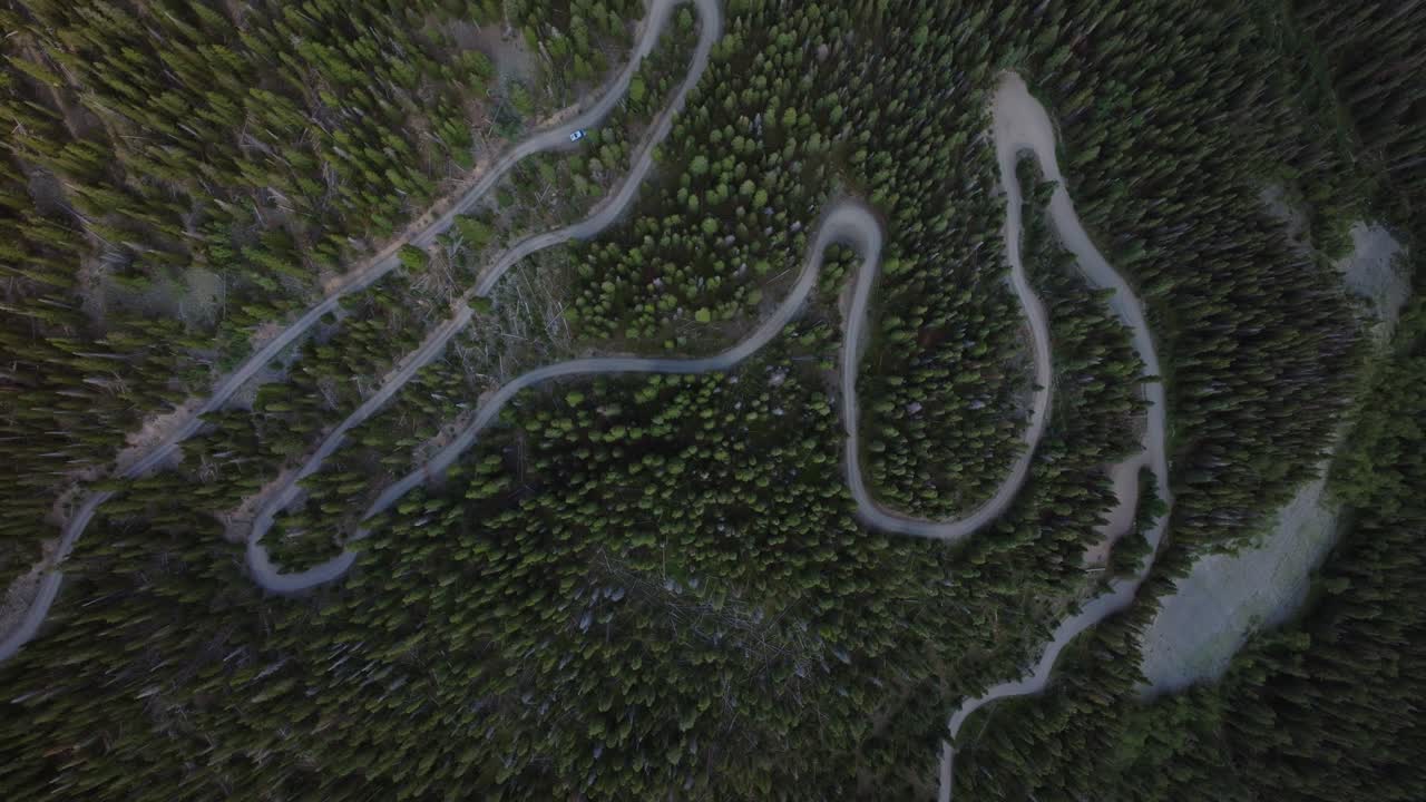 Serpentine mountain road winds tightly through steep alpine terrain, carving sharp curves