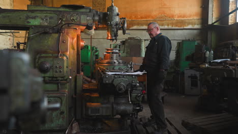 Älterer-Arbeiter-Mit-Schnurrbart-Kontrolliert-Die-Arbeit-Der-Bohrmaschine