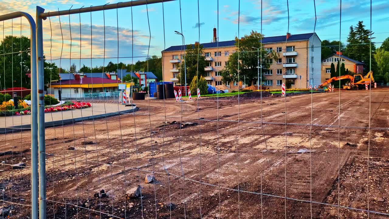 Urban construction site fenced off with machinery and buildings in the background