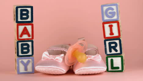 pink soother falling onto baby shoes besides baby blocks