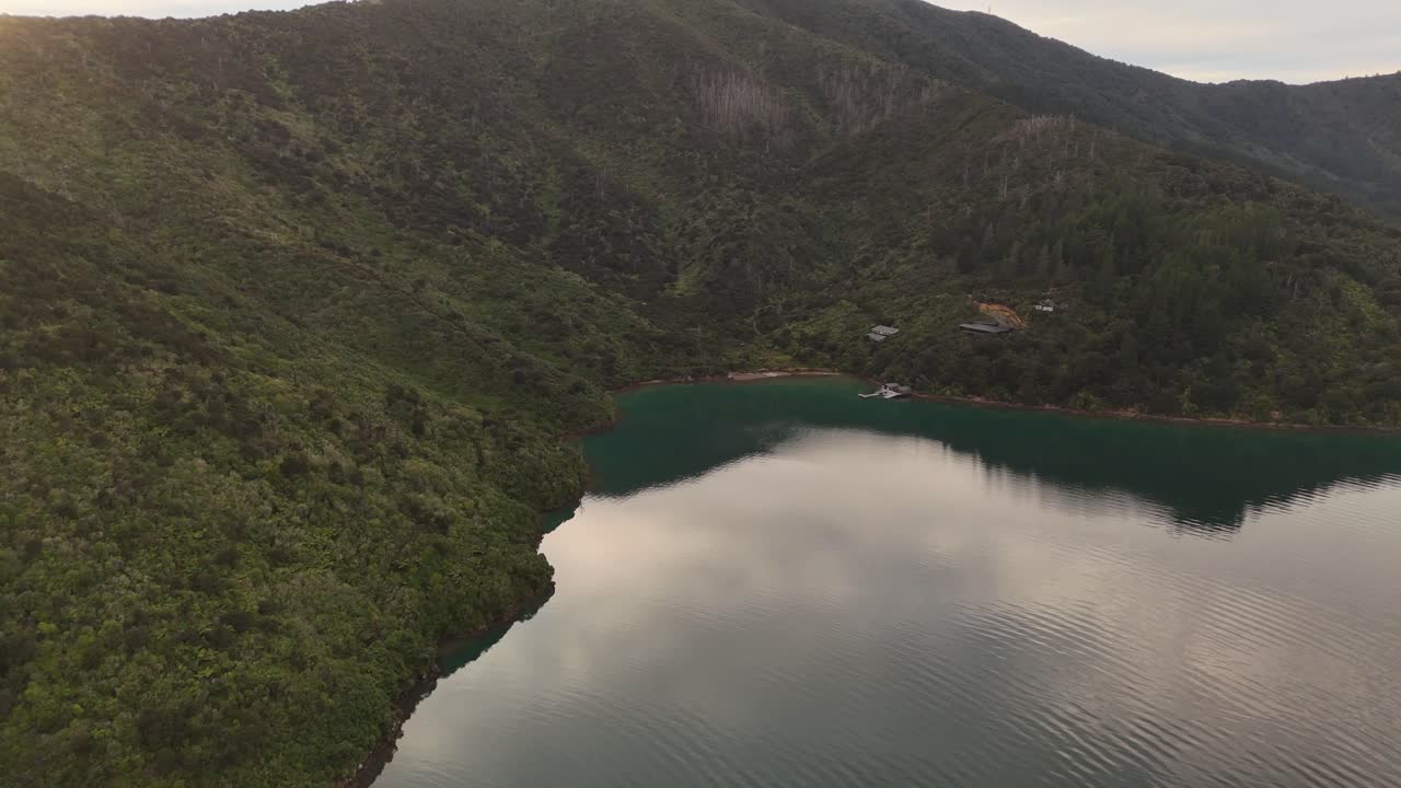 House at waterfront of lake in picton area, New Zealand. Giant Mountains and hills on South Island during dusk scene. Aerial approaching shot. Peaceful scene