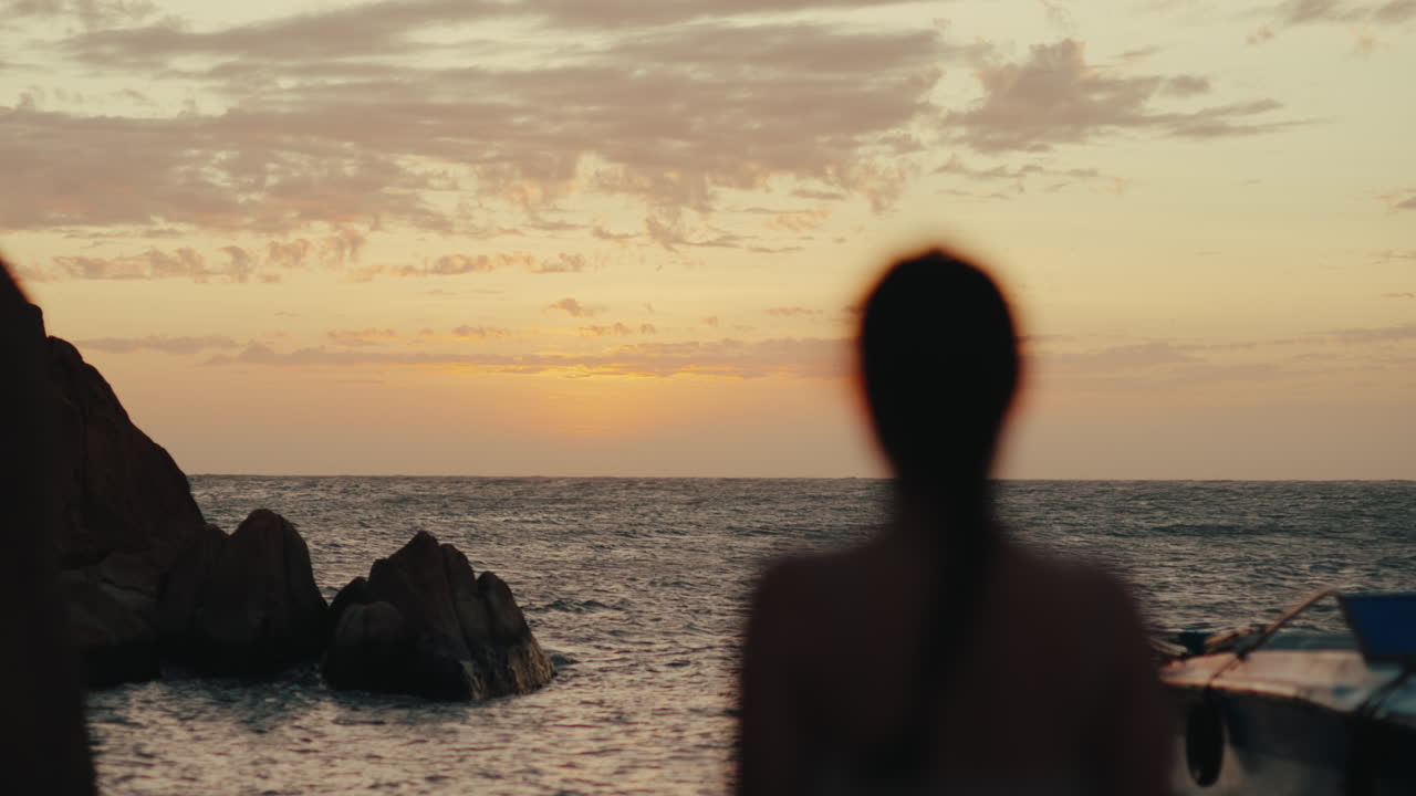 Silhouette sfocata di donna che guarda l'orizzonte dell'oceano con costa rocciosa al tramonto, astratto, cammina da sola.
