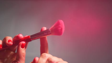 a close-up of a makeup brush picking up red powder from a stack and then being shaken with fingers, releasing powder dust, embodies the concept of makeup and beauty in lifestyle