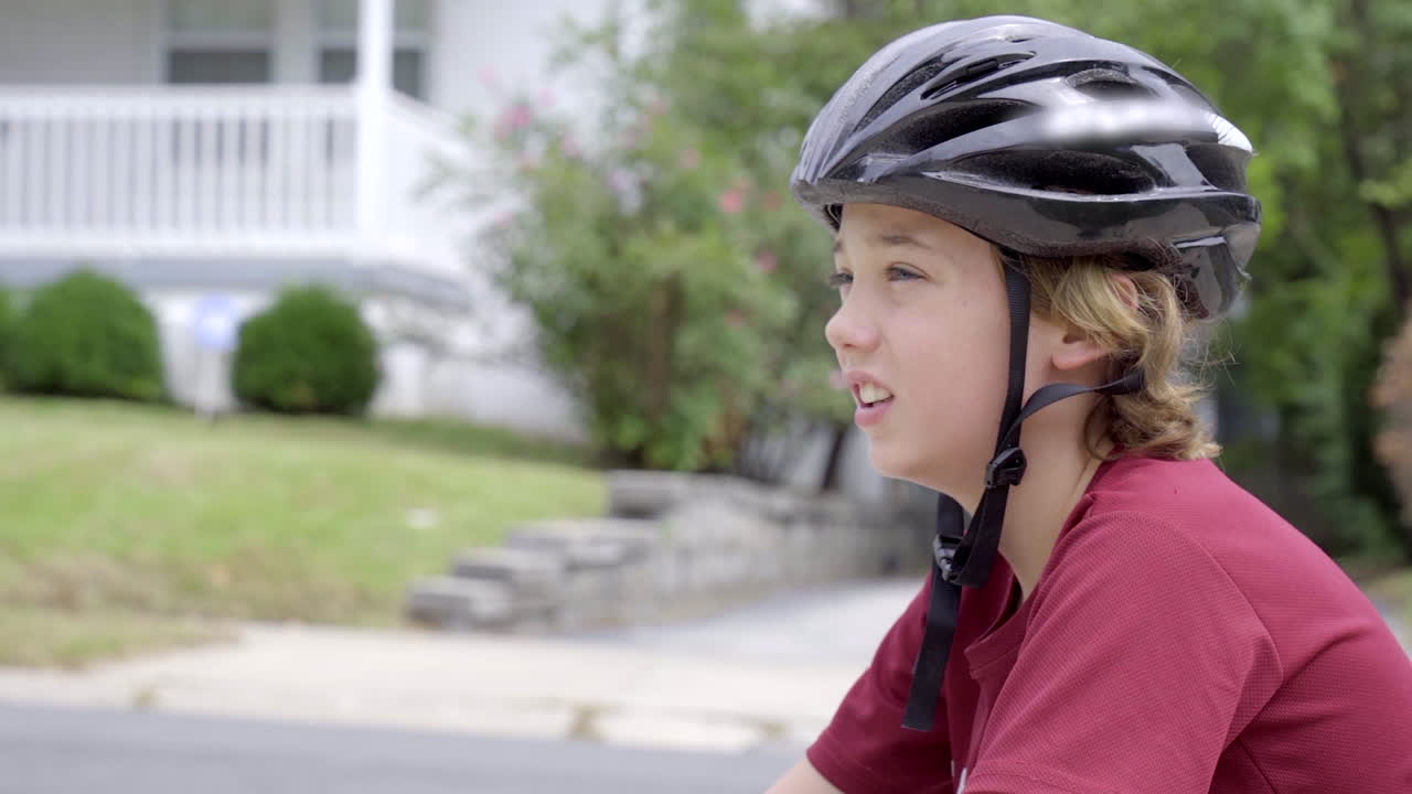 Cute boy wearing a bike helmet looks up the road from the driveway