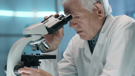 científico anciano usando el microscopio y tomando notas