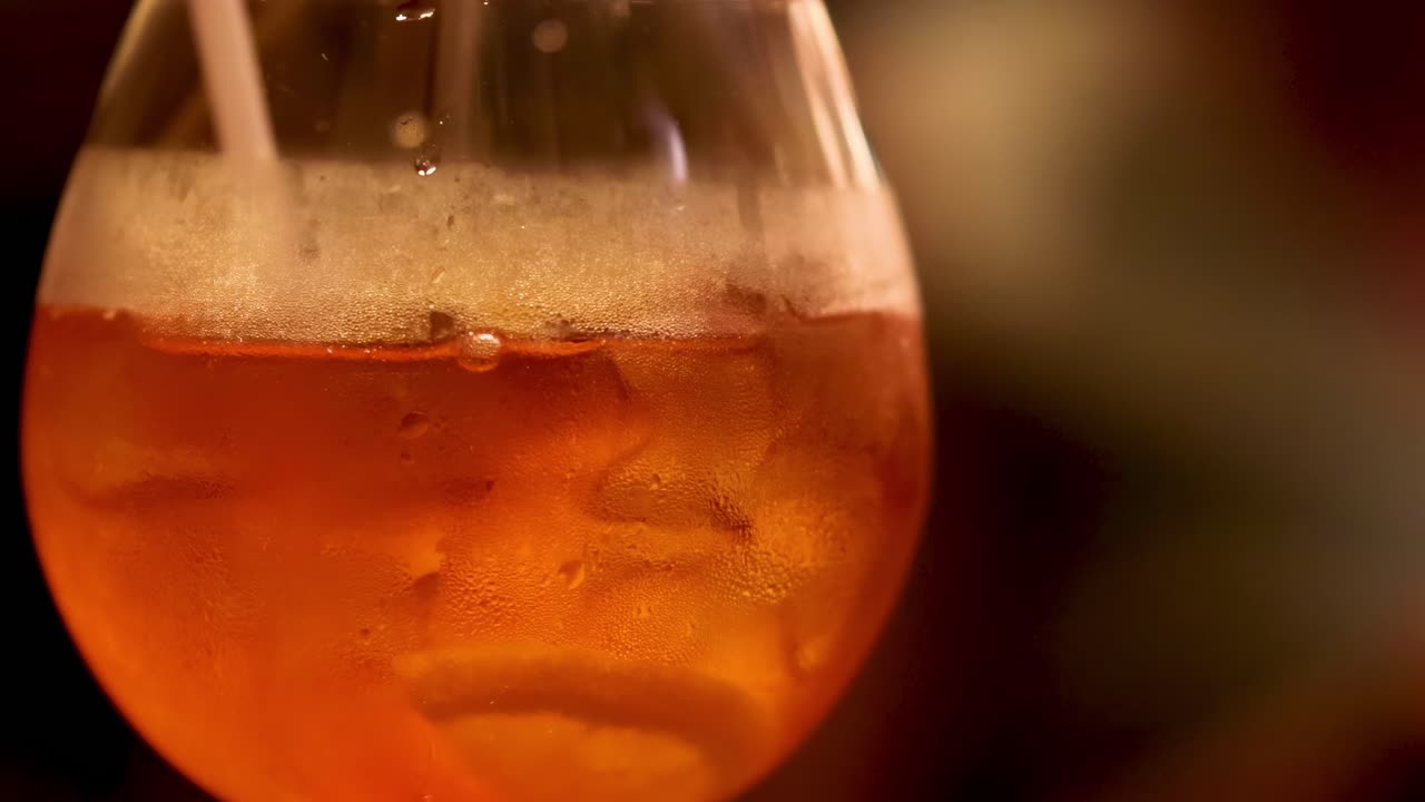 Una vista ravvicinata di un cocktail arancione mescolato con una cannuccia, che evidenzia bolle e ghiaccio