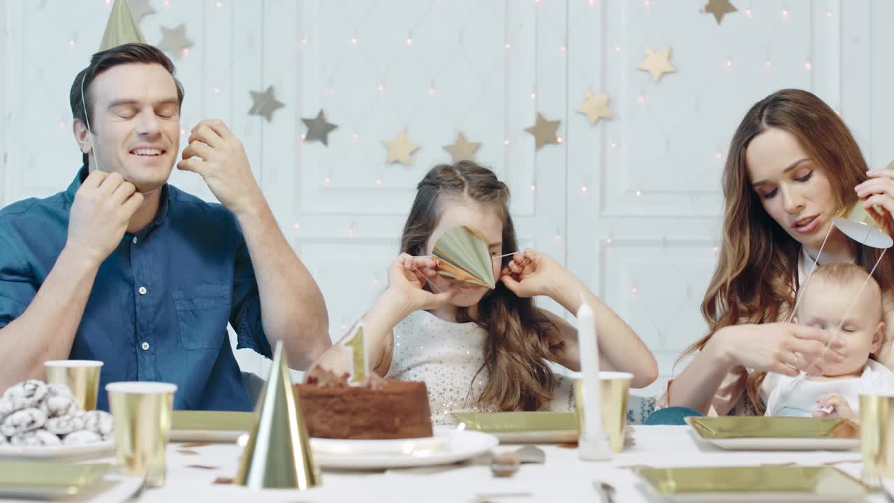 럭셔리 하우스에서 파티 모자를 놓고 재 ⁇ 는 가족. 두 아이를 가진 행복한 커플