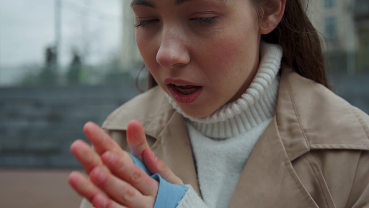 Close up of woman wearing beige coat and white turtleneck hands clasped together in prayer gesture. Soft lighting highlights texture details on clothing fabric. Urban background with blurred