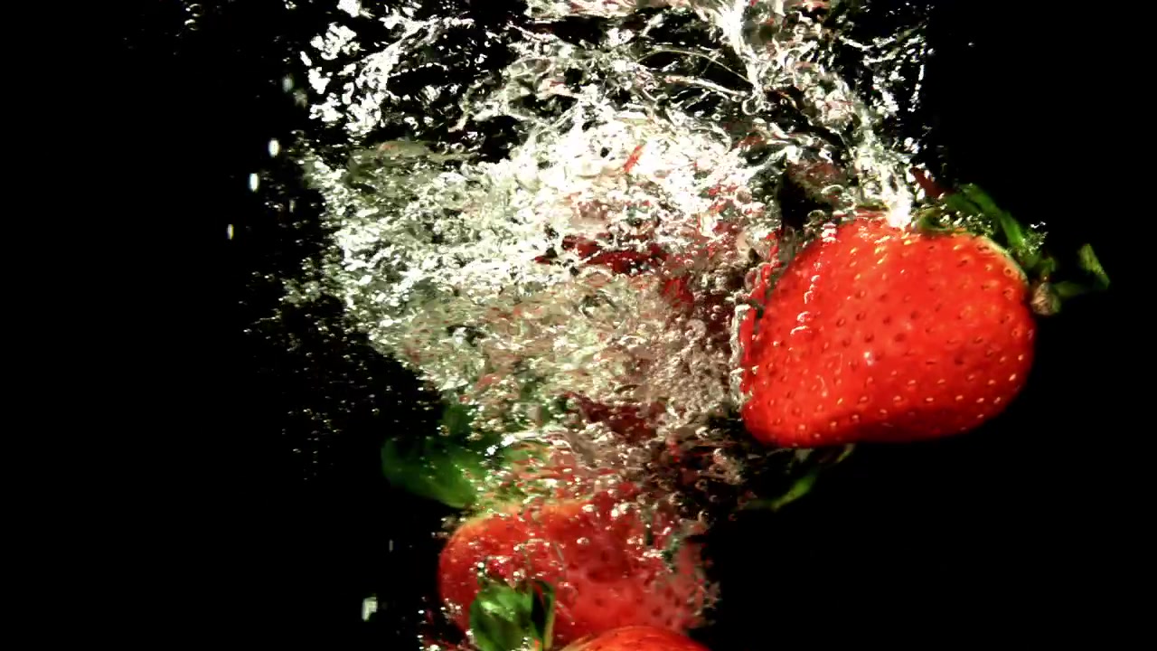 Frische rote Erdbeeren tauchen in Zeitlupe ins Wasser ein