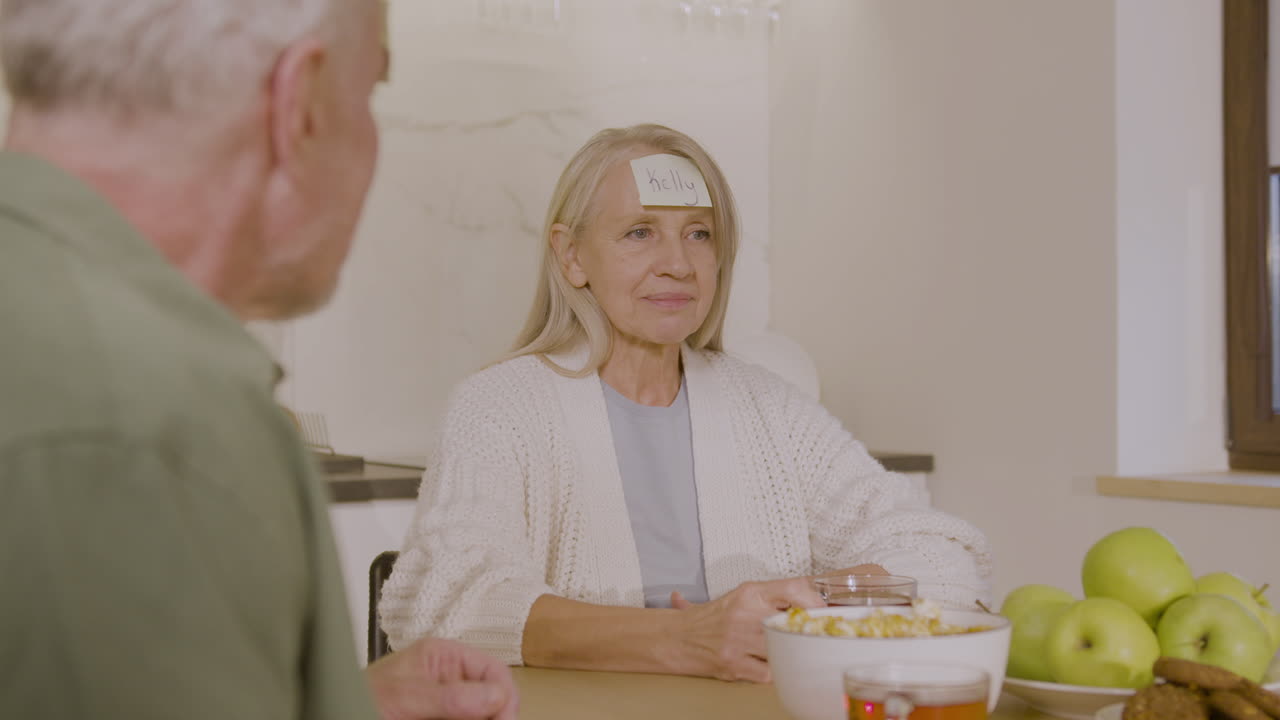 이마 2에 부착된 끈적끈적한 종이로 누가 게임을 하는지 추측하는 행복한 고위 여성