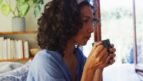 Mixed-race-woman-drinking-coffee-while-sitting-on-the-couch-at-home