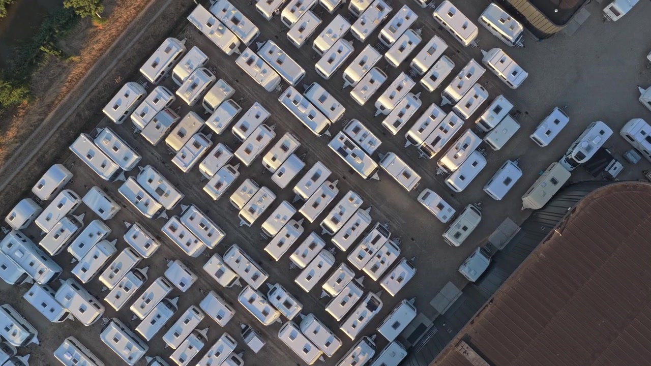 Vista aerea dall'alto di numerose roulotte, camper e autocaravan parcheggiati ordinatamente in un ampio deposito durante una giornata di sole nei Paesi Bassi.