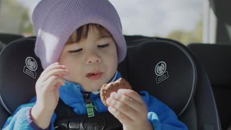 Asian-kid-passenger-rides-in-a-child-car-seat-eating-cookies