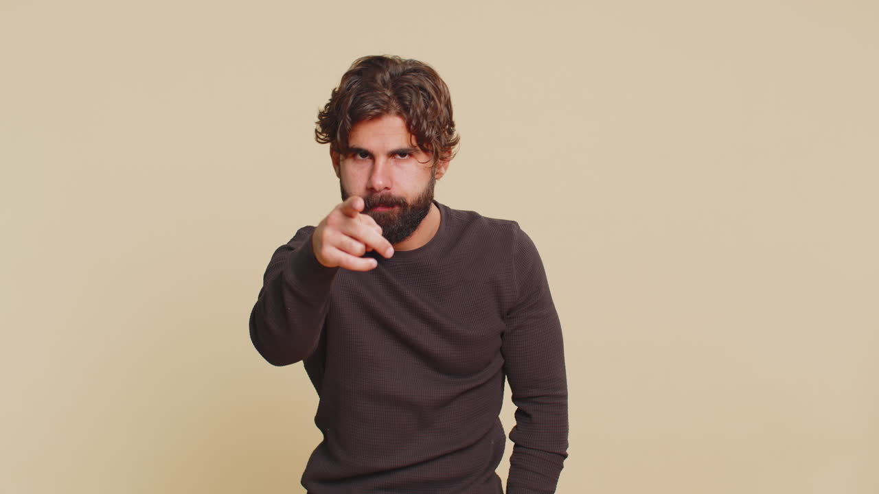 Confident young indian man guy showing i am watching you gesture against beige studio background