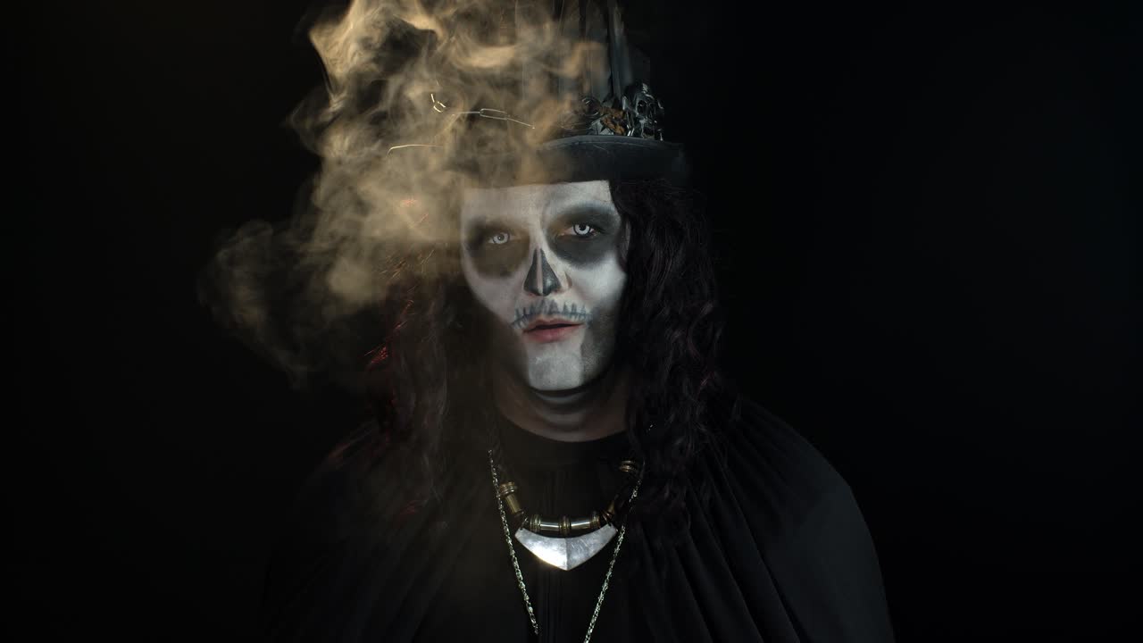 Zlověstný muž s halloweenským make-upem kostlivce vydechuje cigaretový kouř z úst a usmívá se.