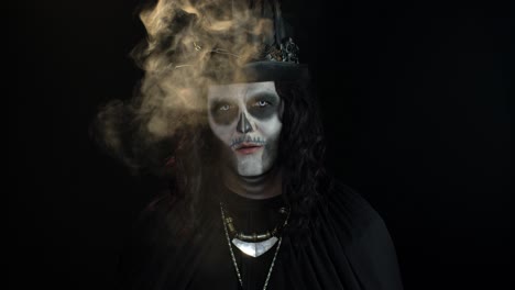 hombre siniestro con maquillaje de esqueleto de halloween exhalando cigarrillo fumando de su boca y sonriendo