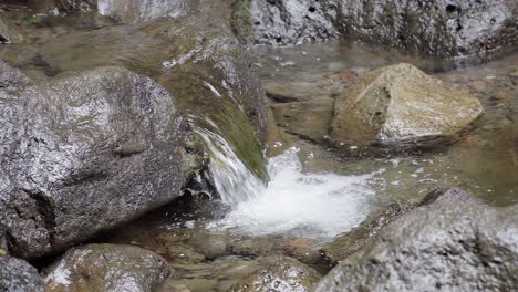 a small stream with black rocks near a waterfall