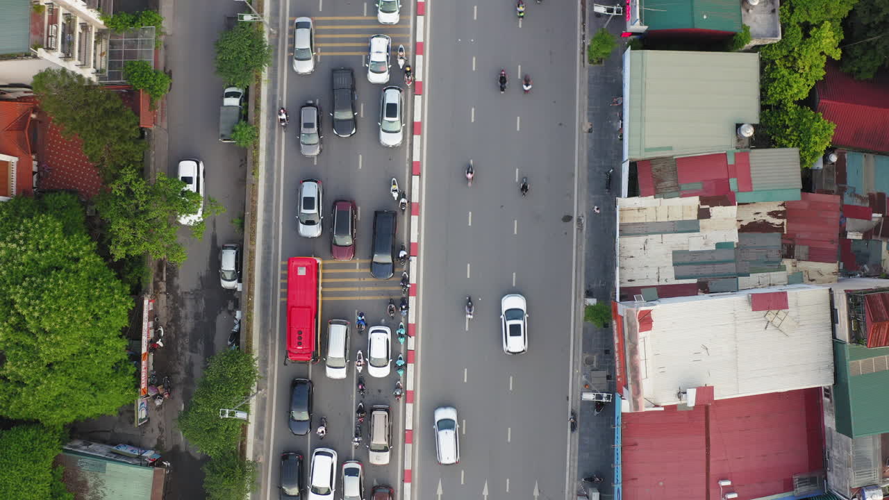 Top-down aerial of Hanoi traffic on Âu Cơ street. Cars and motorbikes flow beside urban rooftops, capturing the city's pulse, density, and daily rhythm.