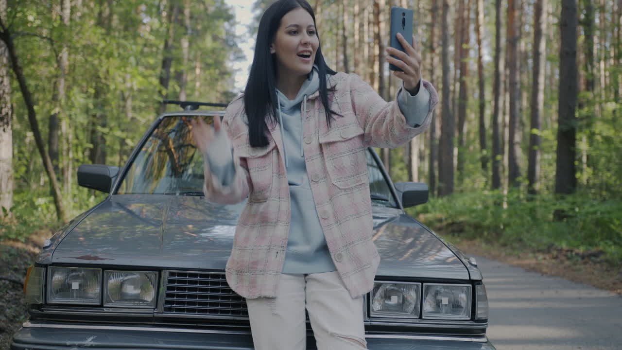Woman taking a selfie by a vintage car in the forest