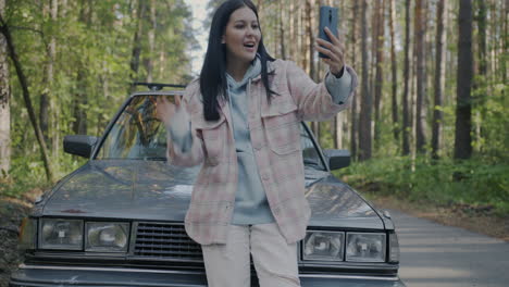 woman taking a selfie by a vintage car in the forest