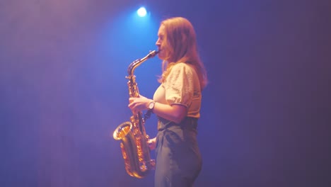 mujer tocando el saxofón en la neblina bajo las luces del escenario