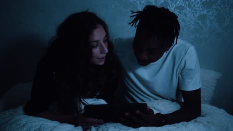 couple watching a tablet device reacting, nodding and talking while sat in bed at night