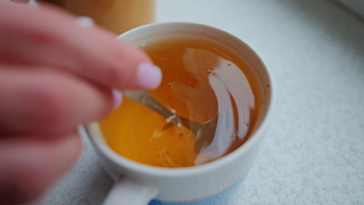Un primo piano al rallentatore mostra del miele dorato che si scioglie delicatamente in una tisana calda