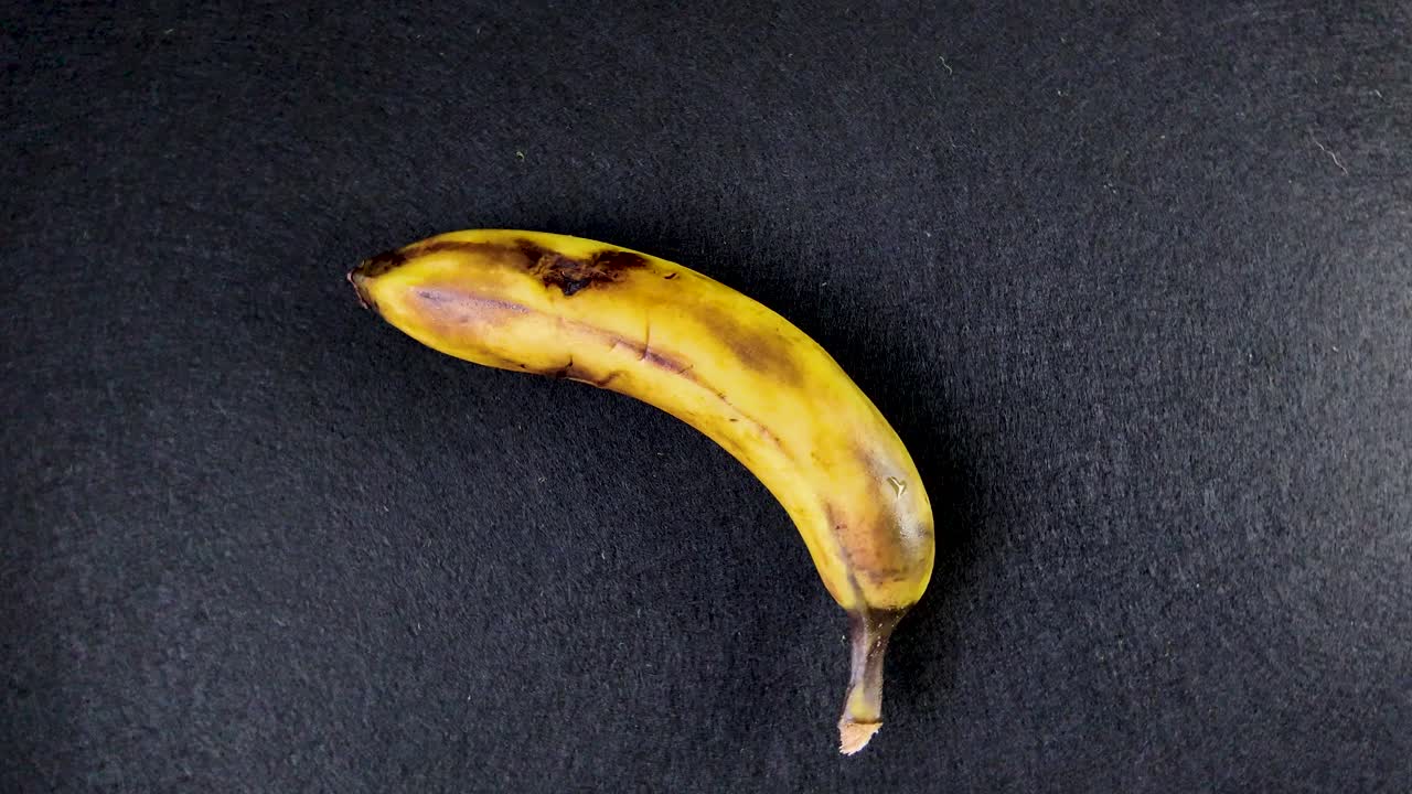 Banana rotating steadily on seamless black background for product, ad, or packaging visuals, top down