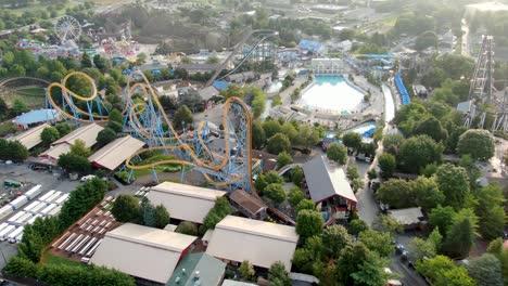 aerial descending turning shot of amusement park roller coaster rides and water park on bright sunny summer morning