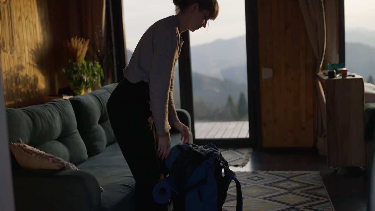 Woman packing backpack in cabin with mountain view